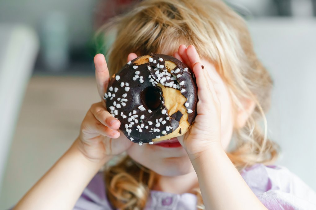Ein Mädchen hält sich einen Donut vor ihr Gesicht.