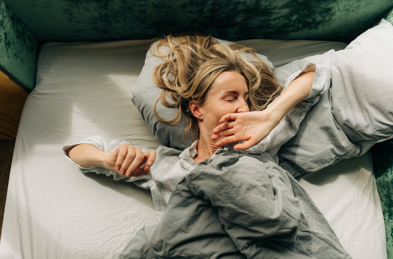 A woman stretches after waking up and yawns while lying in bed.