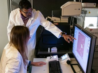 Precision biology for precision medicine: The scientists at the CPI work on research results using ultra-modern methods. A female scientist is sitting in front of a screen, which shows a research result. A male scientist stands next to it and points at the screens.